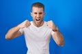 Young caucasian man standing over blue background angry and mad raising fists frustrated and furious while shouting with anger Royalty Free Stock Photo