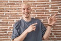 Young caucasian man standing over bricks wall smiling and looking at the camera pointing with two hands and fingers to the side Royalty Free Stock Photo