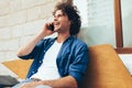 Young Caucasian man stitting on the bench outdoors and talking on mobile phone. Happy male with curly hair resting outside making Royalty Free Stock Photo