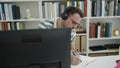 Young caucasian man student using computer taking notes at library university Royalty Free Stock Photo