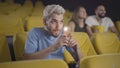 Young Caucasian man taking photo of screen in movie theater. Portrait of handsome criminal breaking rules of cinema