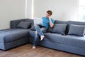 Young Caucasian man is thinking and searching online social media with laptop. He is sitting on sofa in living room. Work from Royalty Free Stock Photo