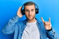 Young caucasian man using headphones and doing rock symbol relaxed with serious expression on face Royalty Free Stock Photo