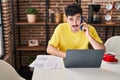 Young caucasian man using laptop talking on smartphone at home Royalty Free Stock Photo