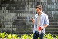 Young caucasian man using smartphone  holding the coffee cup and pulling the suitcase waiting his friend for travel together Royalty Free Stock Photo