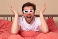 Young caucasian man watching TV at home in the bed in 3d glasses being excited and amuzed Royalty Free Stock Photo