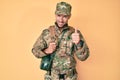 Young caucasian man wearing camouflage army uniform and canteen smiling happy and positive, thumb up doing excellent and approval Royalty Free Stock Photo