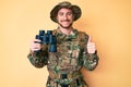 Young caucasian man wearing camouflage army uniform holding binoculars smiling happy and positive, thumb up doing excellent and Royalty Free Stock Photo