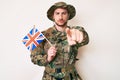 Young caucasian man wearing camouflage army uniform holding united kingdom flag pointing with finger to the camera and to you, Royalty Free Stock Photo