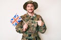 Young caucasian man wearing camouflage army uniform holding united kingdom flag pointing finger to one self smiling happy and Royalty Free Stock Photo