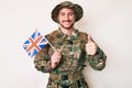 Young caucasian man wearing camouflage army uniform holding united kingdom flag smiling happy and positive, thumb up doing Royalty Free Stock Photo