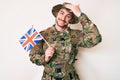 Young caucasian man wearing camouflage army uniform holding united kingdom flag stressed and frustrated with hand on head, Royalty Free Stock Photo