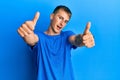 Young caucasian man wearing casual blue t shirt approving doing positive gesture with hand, thumbs up smiling and happy for Royalty Free Stock Photo