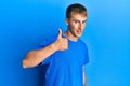 Young caucasian man wearing casual blue t shirt doing happy thumbs up gesture with hand Royalty Free Stock Photo