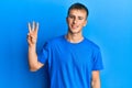 Young caucasian man wearing casual blue t shirt showing and pointing up with fingers number three while smiling confident and Royalty Free Stock Photo