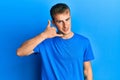 Young caucasian man wearing casual blue t shirt smiling doing phone gesture with hand and fingers like talking on the telephone Royalty Free Stock Photo