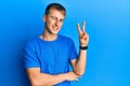 Young caucasian man wearing casual blue t shirt smiling with happy face winking at the camera doing victory sign with fingers Royalty Free Stock Photo