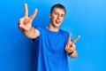 Young caucasian man wearing casual blue t shirt smiling with tongue out showing fingers of both hands doing victory sign Royalty Free Stock Photo