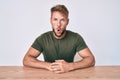 Young caucasian man wearing casual clothes sitting on the table afraid and shocked with surprise expression, fear and excited face Royalty Free Stock Photo