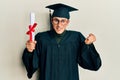 Young caucasian man wearing graduation cap and ceremony robe holding diploma screaming proud, celebrating victory and success very Royalty Free Stock Photo