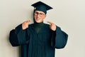 Young caucasian man wearing graduation cap and ceremony robe smiling cheerful showing and pointing with fingers teeth and mouth Royalty Free Stock Photo