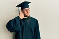 Young caucasian man wearing graduation cap and ceremony robe smiling doing phone gesture with hand and fingers like talking on the Royalty Free Stock Photo