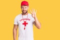 Young caucasian man wearing lifeguard t shirt holding whistle showing and pointing up with fingers number four while smiling