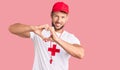 Young caucasian man wearing lifeguard t shirt holding whistle smiling in love doing heart symbol shape with hands