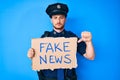 Young caucasian man wearing police uniform holding fake news banner with angry face, negative sign showing dislike with thumbs