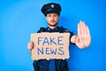 Young caucasian man wearing police uniform holding fake news banner with open hand doing stop sign with serious and confident Royalty Free Stock Photo