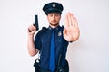 Young caucasian man wearing police uniform holding gun with open hand doing stop sign with serious and confident expression, Royalty Free Stock Photo