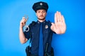 Young caucasian man wearing police uniform holding handcuffs with open hand doing stop sign with serious and confident expression, Royalty Free Stock Photo