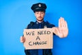 Young caucasian man wearing police uniform holding we need a change banner with open hand doing stop sign with serious and Royalty Free Stock Photo