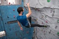 Young caucasian man wearing protective face mask rappelling at indoor artificial rock climbing wall Royalty Free Stock Photo