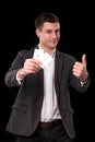 Young caucasian man wearing suit holding two aces in his hand and showing thumb up hand gesture with smile on black Royalty Free Stock Photo