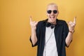 Young caucasian man wearing sunglasses standing over yellow background shouting with crazy expression doing rock symbol with hands Royalty Free Stock Photo