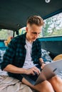 Young caucasian man work on computer sitting in a van, freelancer using laptop during traveling