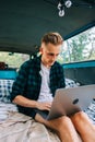 Young caucasian man work on computer sitting in a van, freelancer using laptop during traveling