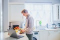 Young caucasian man working from home. Freelancer cooking vegetarian lunch on the kitchen table and working on pc laptop Royalty Free Stock Photo