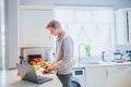 Young caucasian man working from home. Freelancer cooking vegetarian lunch on the kitchen table and working on pc laptop. Home Royalty Free Stock Photo