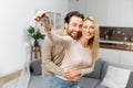 Young caucasian married couple homeowners smiling, showing keys from a new apartment, hugging and looking at the camera Royalty Free Stock Photo