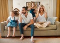 Young caucasian mother and father suffering a headache with their daughters playing jumping on the couch in the lounge