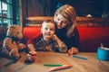 Young Caucasian mother and son sitting in restaurant drawing with colored pencils on craft brown paper. Family together in a cafe Royalty Free Stock Photo