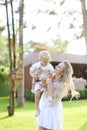 Young caucasian mother walking with babe on grass in yard.