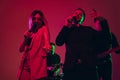 Young caucasian musicians, singers performing in neon light on red studio background