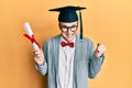 Young caucasian nerd man wearing glasses and graduation cap and holding degree screaming proud, celebrating victory and success Royalty Free Stock Photo