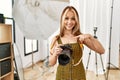 Young caucasian photographer girl holding professional camera at photography studio pointing finger to one self smiling happy and Royalty Free Stock Photo