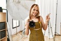 Young caucasian photographer girl holding professional camera at photography studio smiling happy pointing with hand and finger to Royalty Free Stock Photo