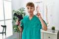 Young caucasian physio man holding muscle percusion gun at the clinic surprised with an idea or question pointing finger with
