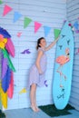 Young caucasian pregnant woman standing near surfboard and decorated children house.